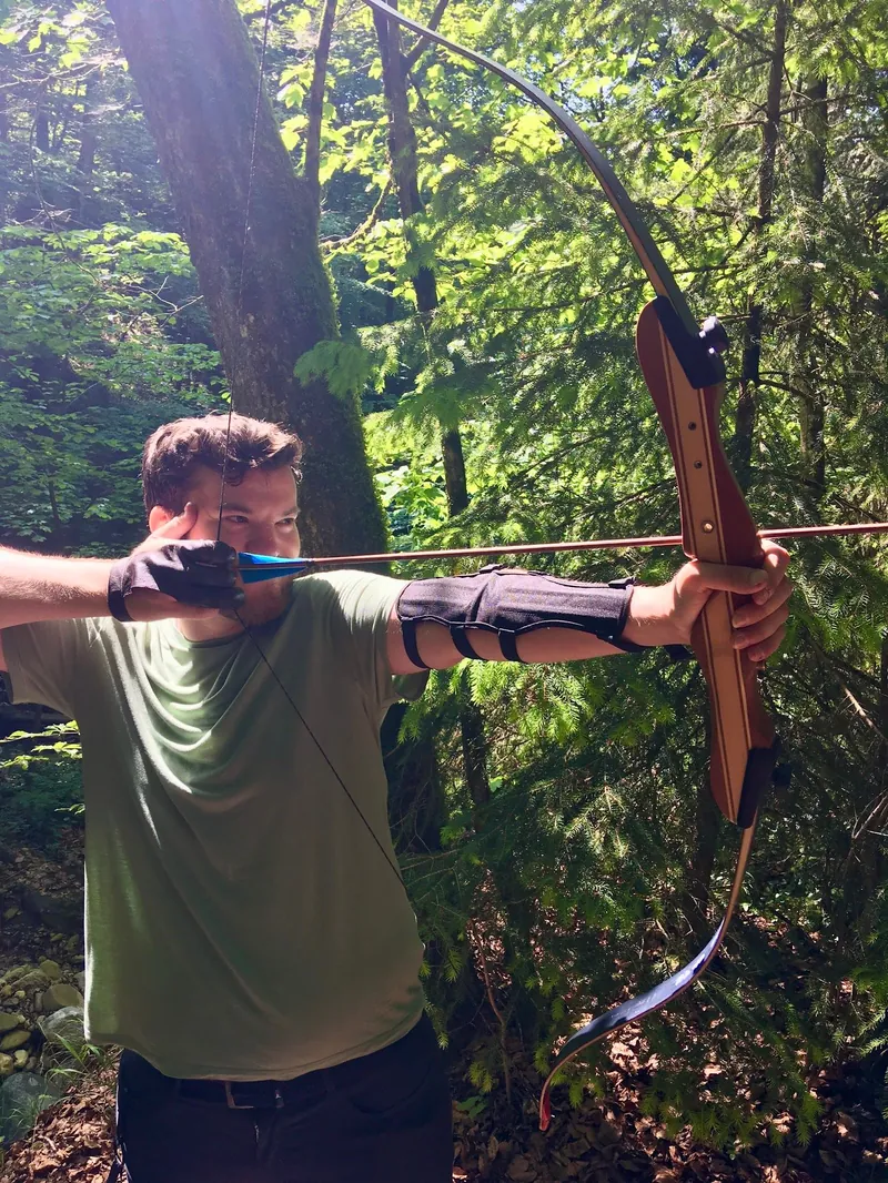 Jakob drawing a bow on a forest archery course.